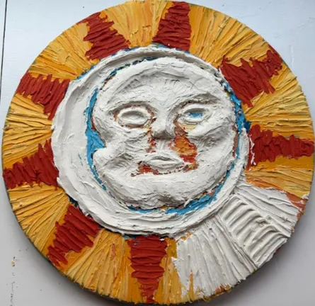 The sun and moon piece in progress: a white spackle face in relief, ringed by rough red and yellow rays.