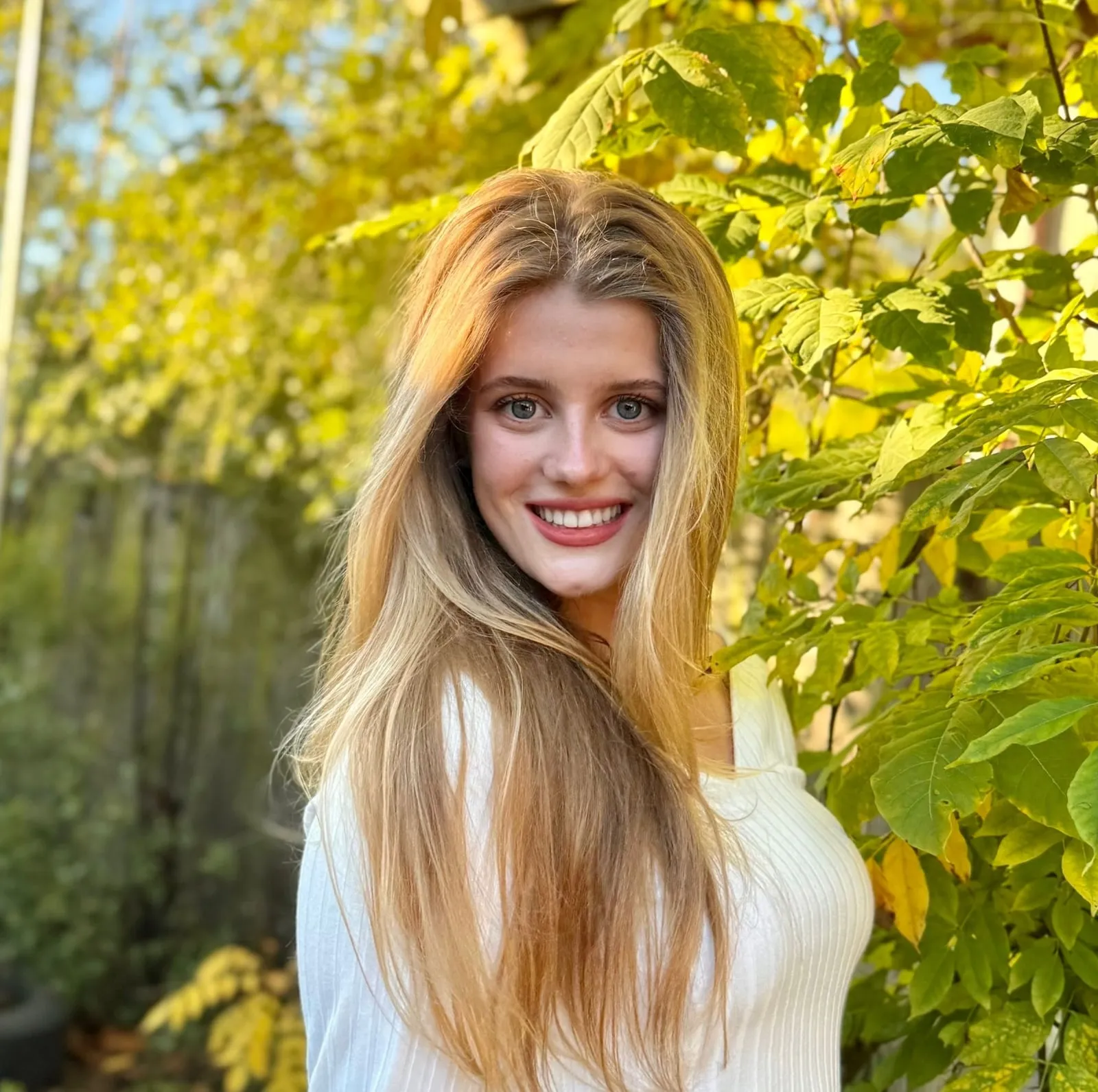 Rachel McGowan, smiling, standing in front of yellow autumn leaves